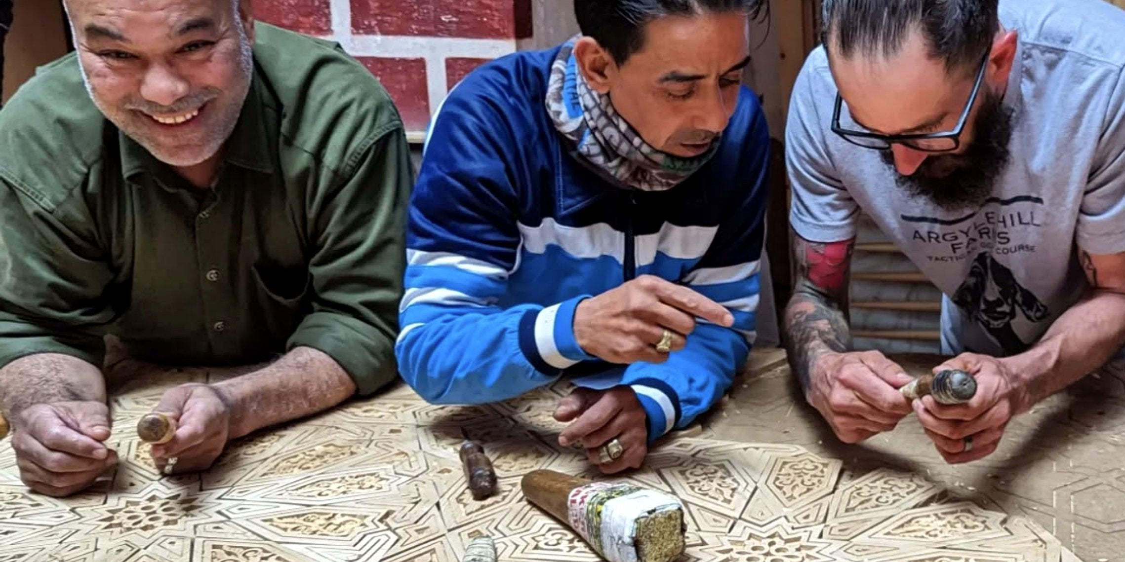 Three craftsmen carving an intricate wooden door panel with hand tools in Marrakesh.